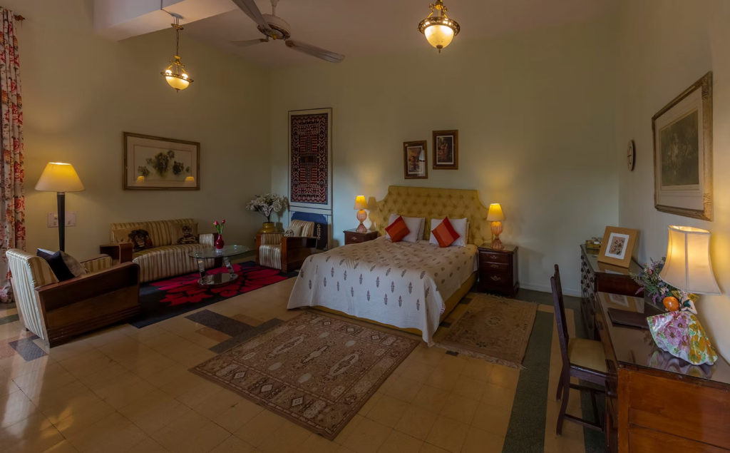 A guest bedroom at Orchard Palace, Gondal, with vintage striped armchairs, patterned rugs and warm lamplight