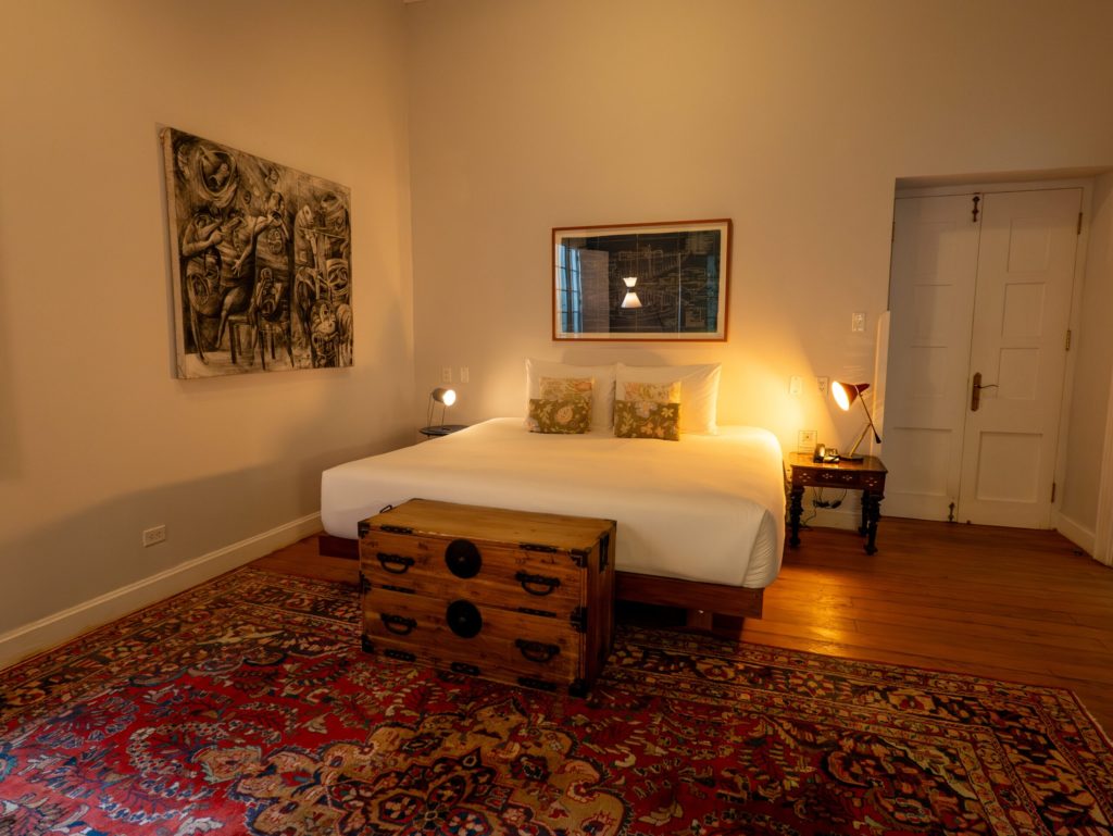 Bedroom with a charcoal figurative artwork, a Japanese tansu chest at the foot of the bed and richly patterned rugs