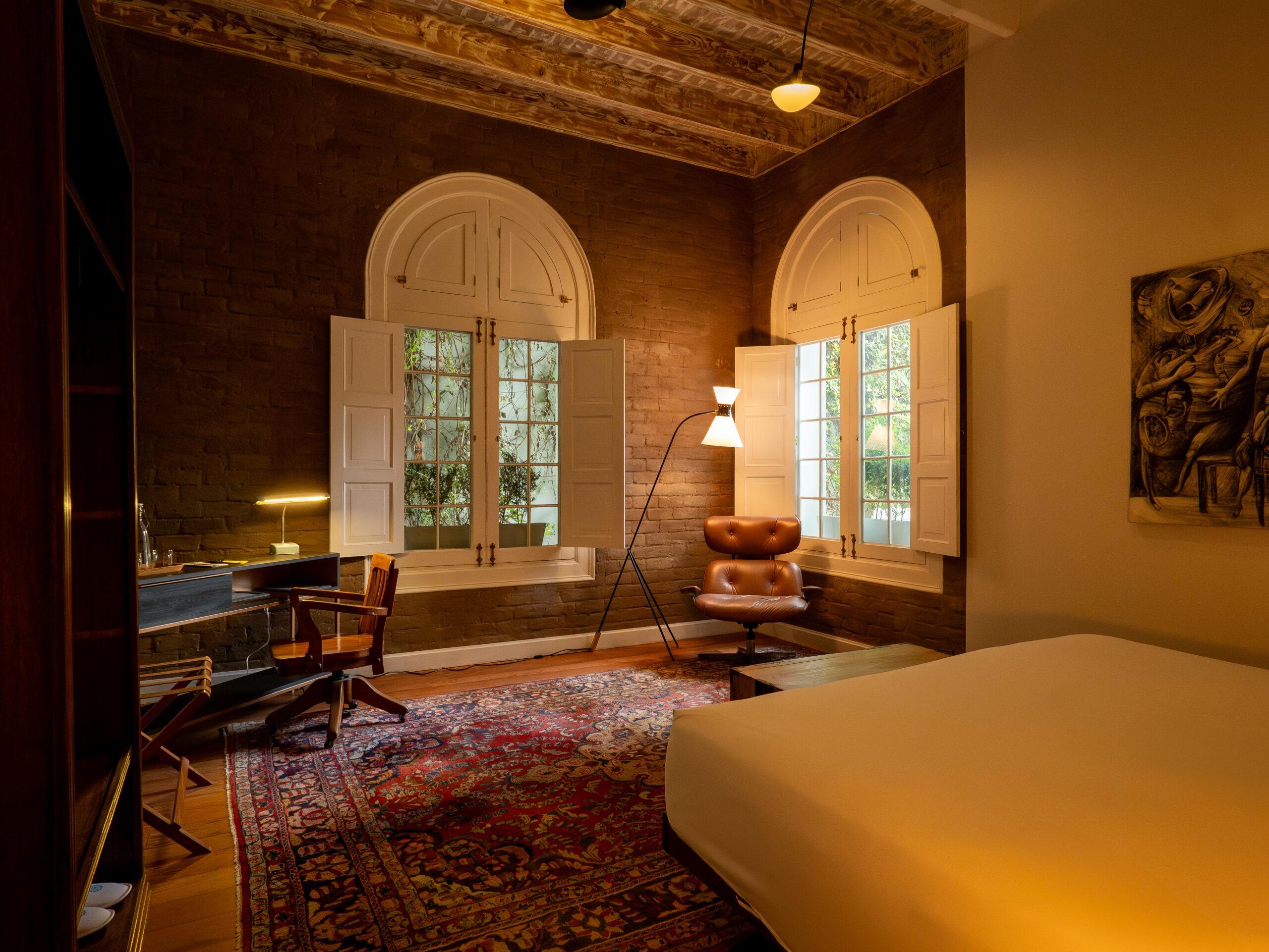 Brick-walled bedroom corner with twin arched windows, a leather swivel chair and antique writing desk