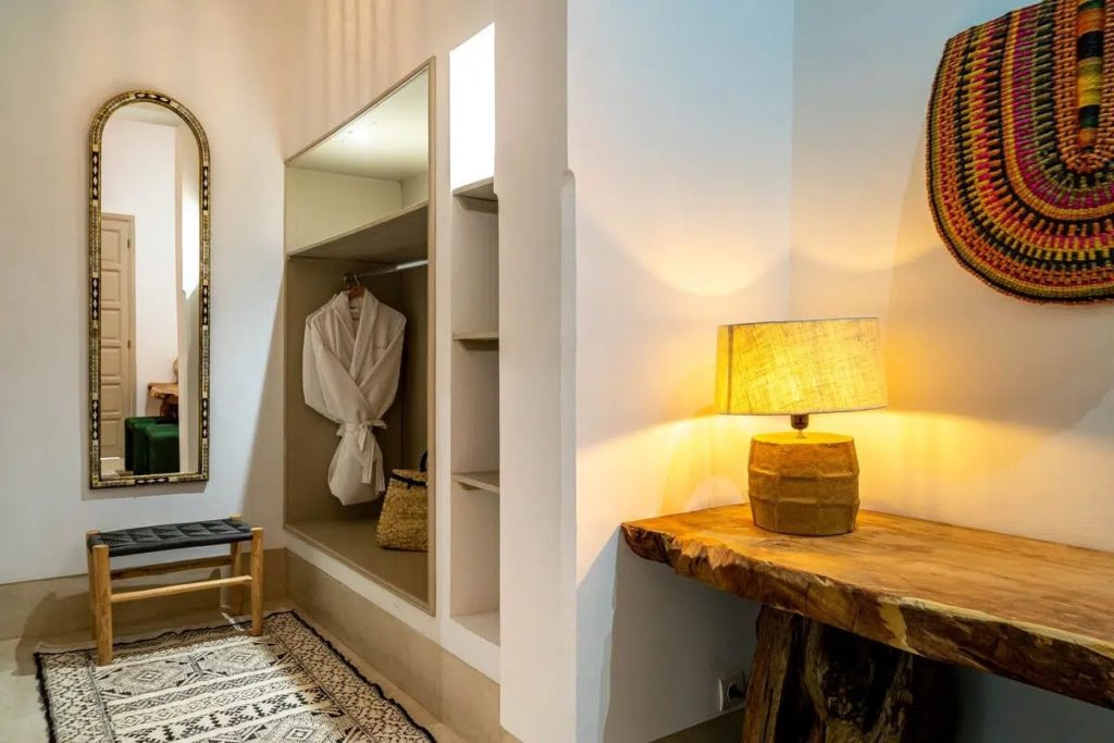 Dressing nook with arched mirror, open wardrobe & woven bench beside a live-edge console