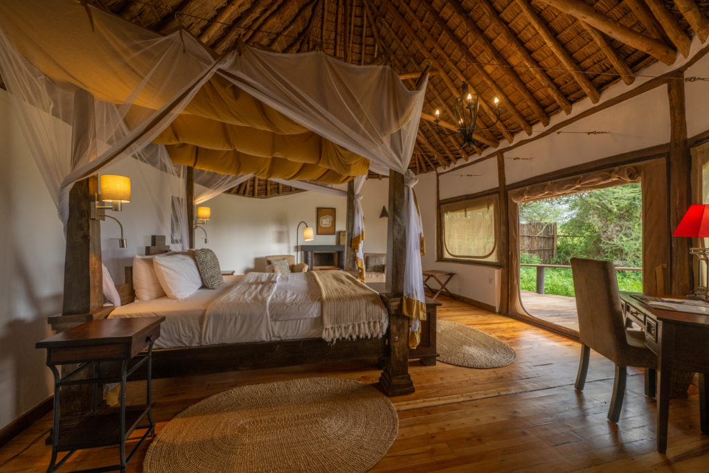 Bedroom with a four-poster bed, mosquito net, writing desk and wooden floors, its canvas wall rolled up onto a private veranda.