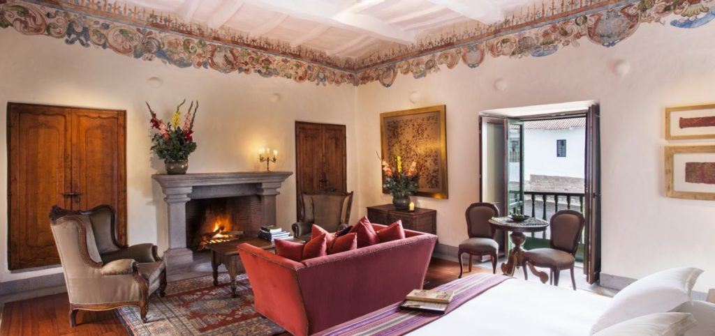 Suite with a decorative painted cornice, stone fireplace and carved wooden doors opening onto a private balcony