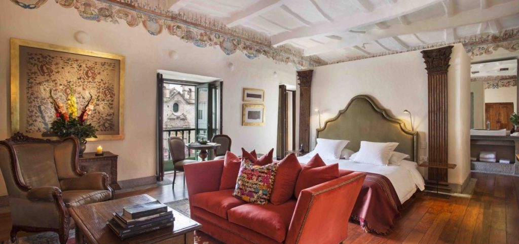 Suite with painted ceiling frieze, a green leather headboard and doors opening onto a Plaza de Armas balcony