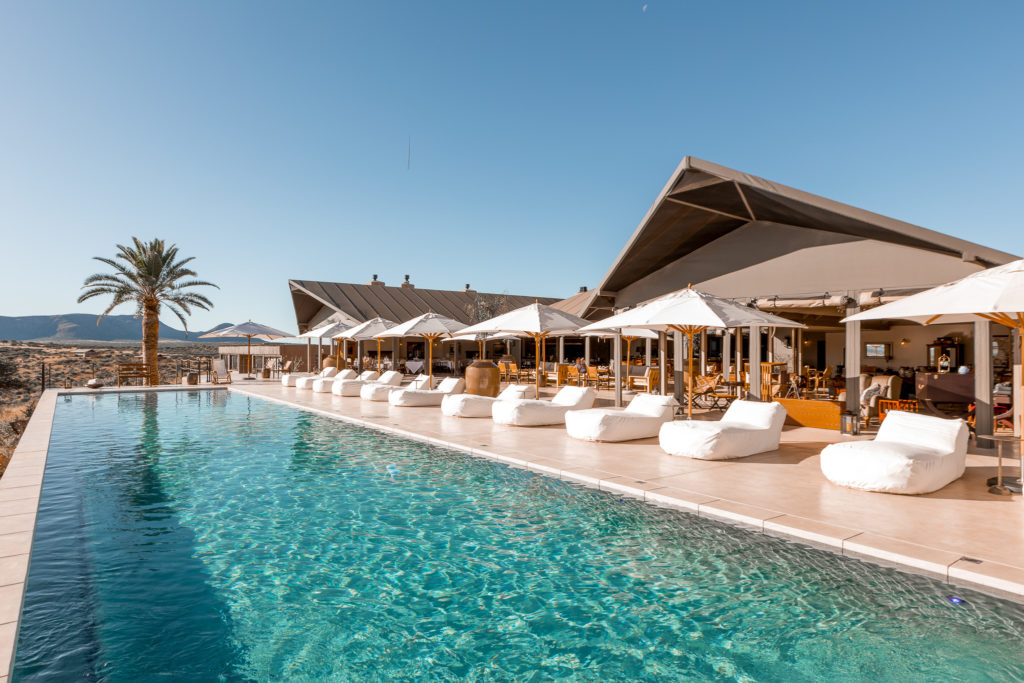Loungers line the infinity pool at Gmundner Lodge, with the main lodge and desert beyond