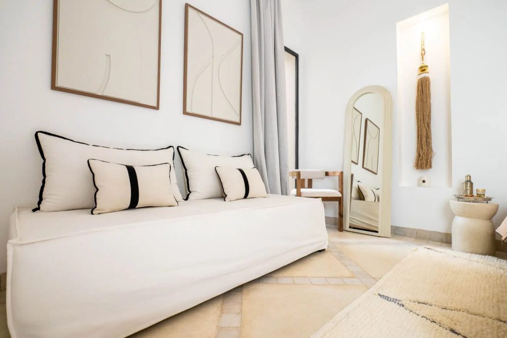 Bedroom daybed with black-trimmed cushions beneath abstract artwork & arched mirror