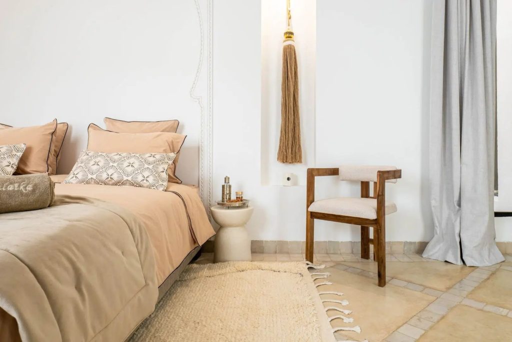 Bedside detail with blush linens, tasselled wall hanging & woven armchair