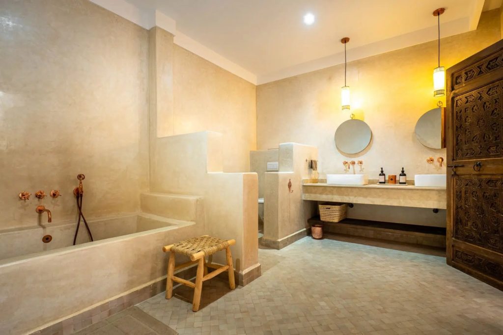 Bathroom with tadelakt bathtub, twin vessel sinks & carved wooden door