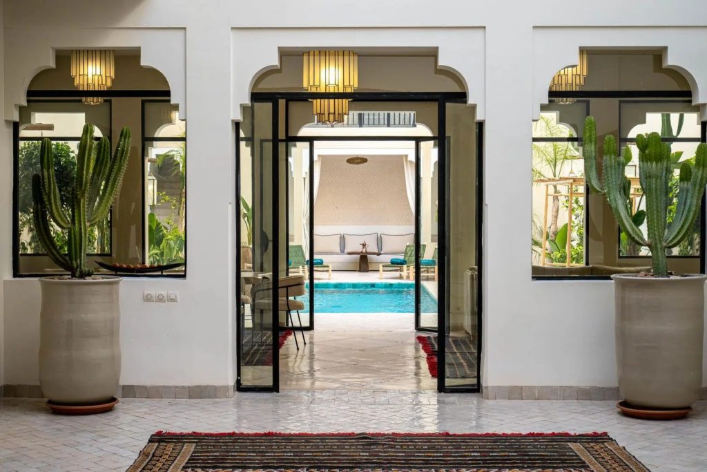 Glass doorway framed by potted cacti opening onto the courtyard pool