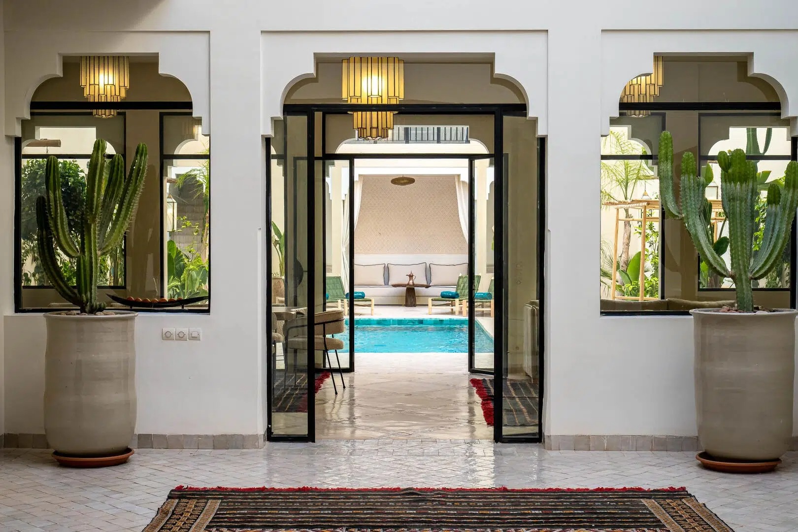 Glass doorway framed by potted cacti opening onto the courtyard pool