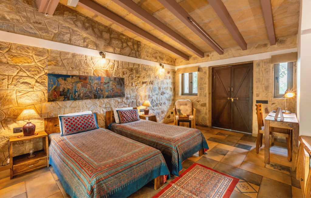 Twin-bedded Safari Cottage room with exposed stone walls and a framed folk-art panel above the beds.
