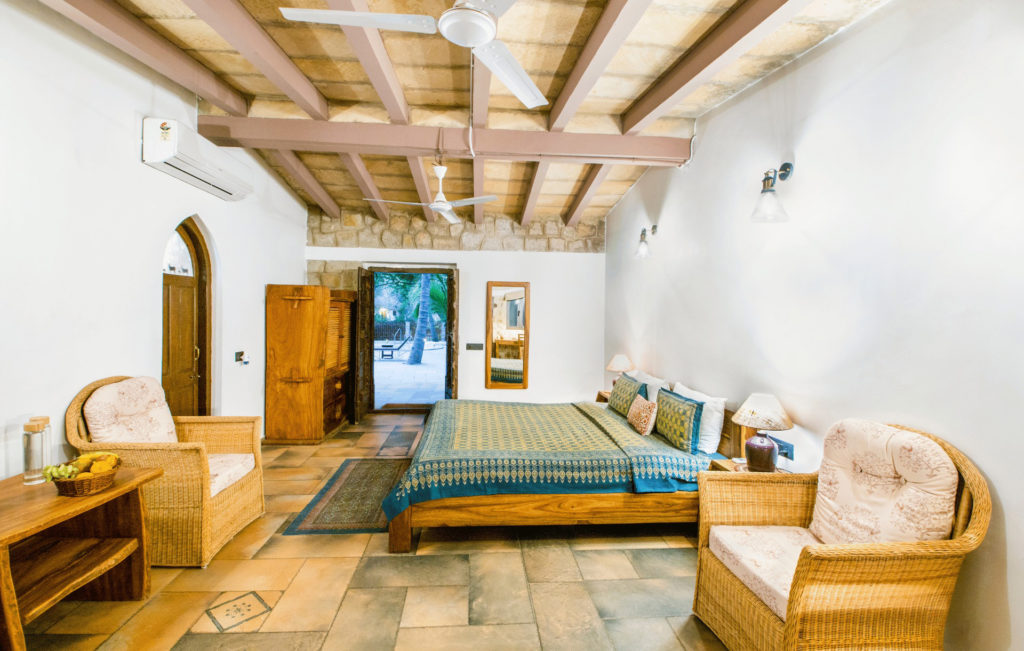 Spacious Safari Cottage bedroom with a poolside terrace, wicker armchairs and a rustic wooden wardrobe.