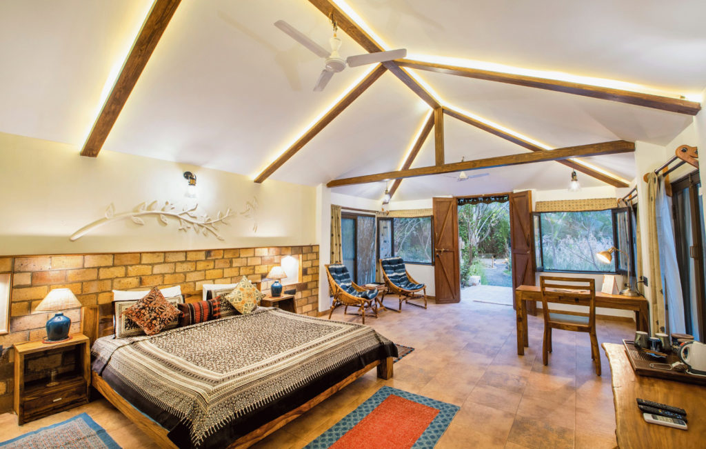 Safari Cottage bedroom with exposed brick headboard wall, vaulted timber ceiling and garden-facing doors.