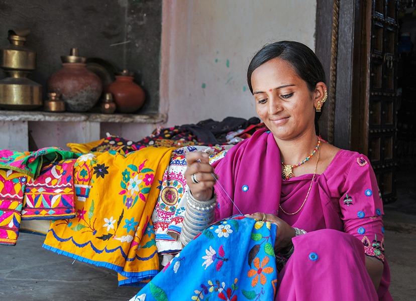 A local artisan hand-embroiders textiles in vivid colour beside displayed craftwork.