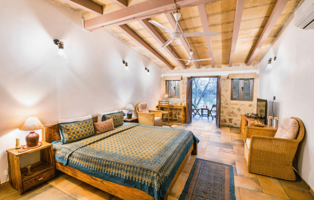 A spacious Dasada Premium Wing bedroom with a lake-facing terrace, exposed beam ceiling and stone walls.