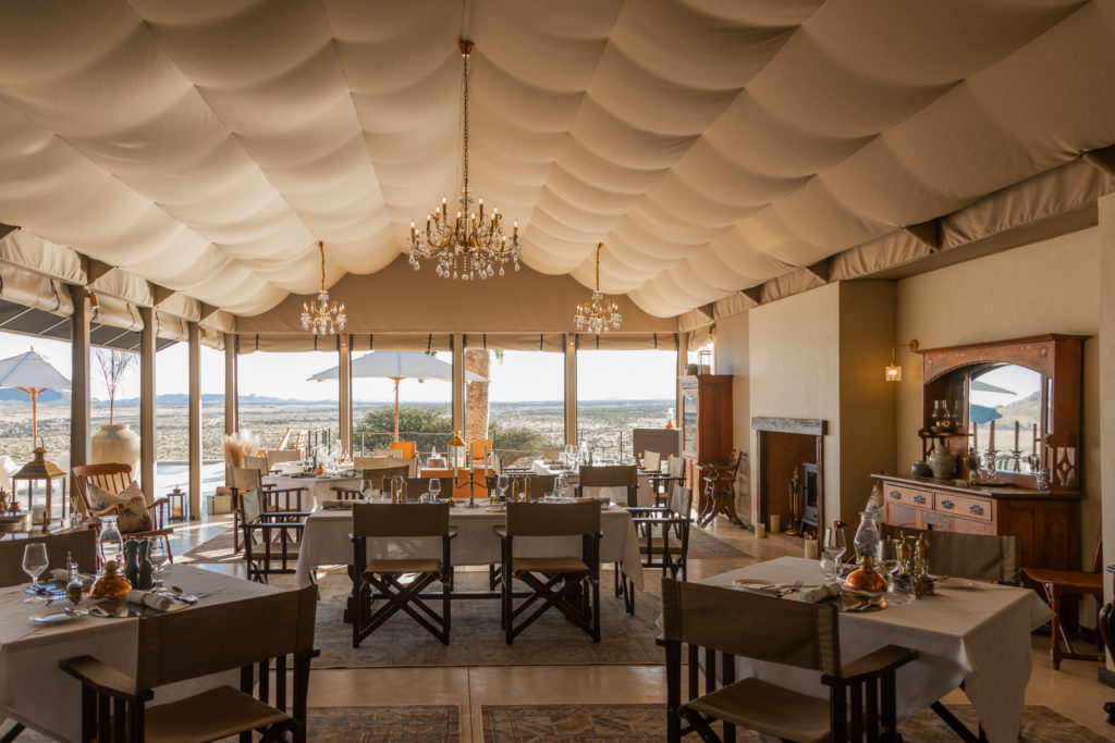 Crystal chandeliers hang above set dining tables at Restaurant Friesacher, framed by desert views