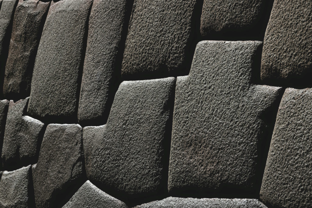 Close-up detail of a precisely fitted Inca stone wall, the large irregular granite blocks interlocking seamlessly without mortar, deep shadows emphasising their texture and craftsmanship, Cusco, Peru.
