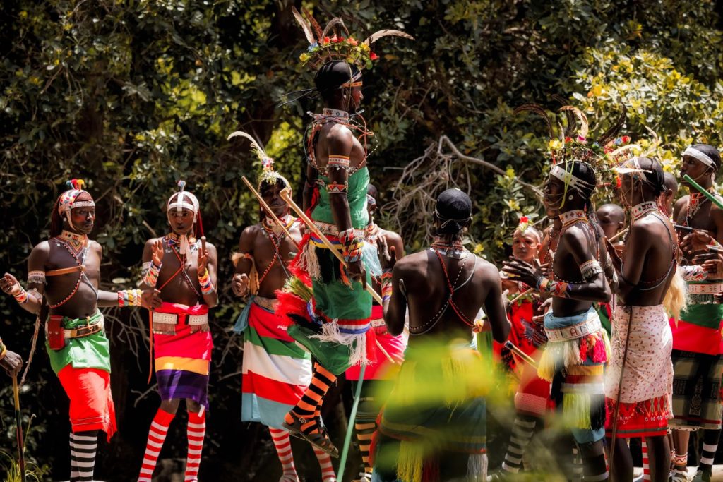 A Samburu dancer leaps high among clapping warriors in feathered headdresses and beadwork during a performance in northern Kenya.
