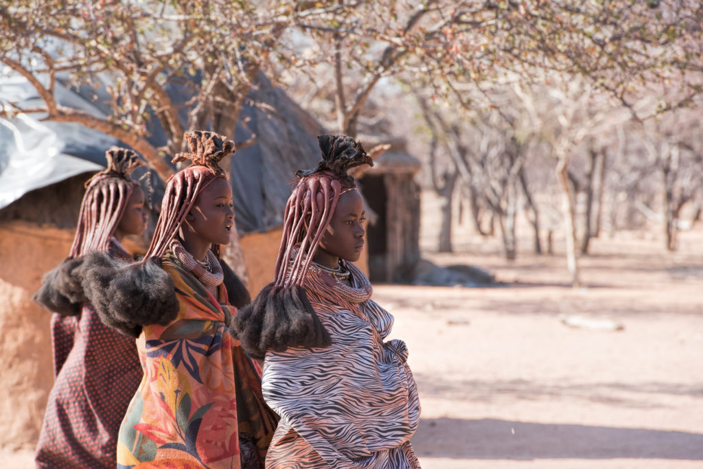 Himba women in traditional dress and ochre-braided hair standing in their village