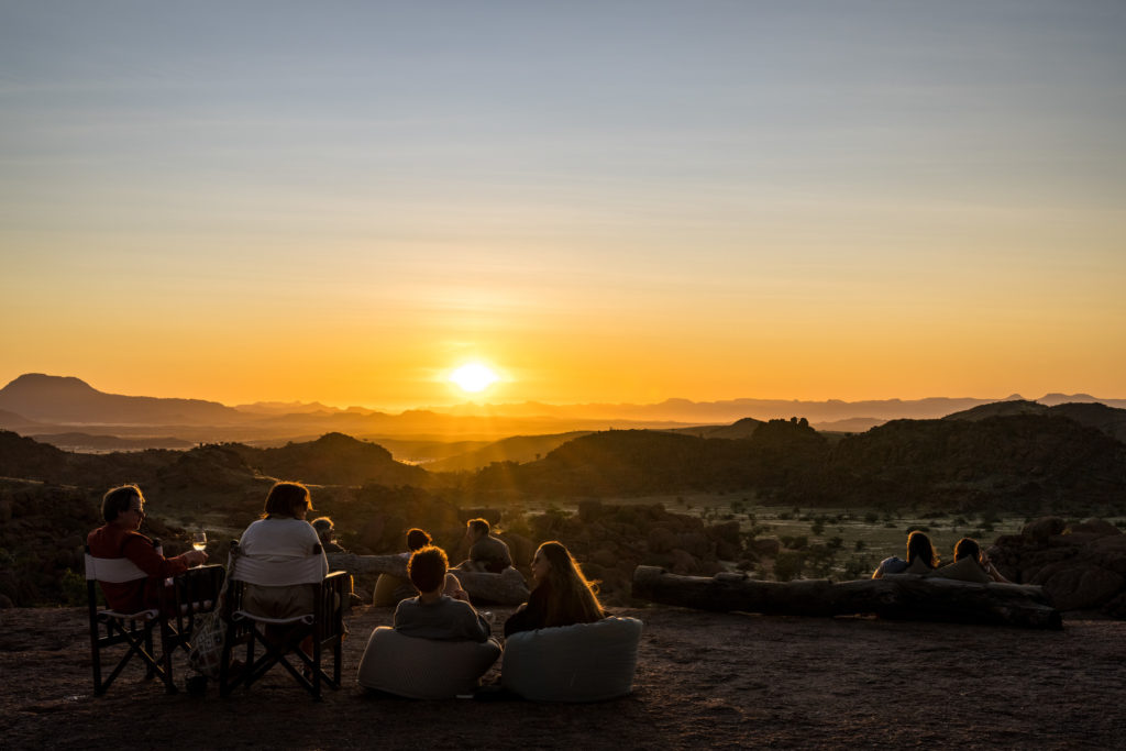 Guests gathered on a rocky outcrop watching the sunset over Damaraland