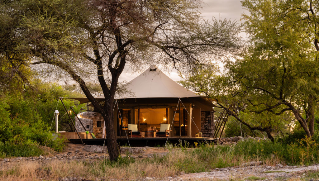 A thatched guest tent lit at dusk, set among trees
