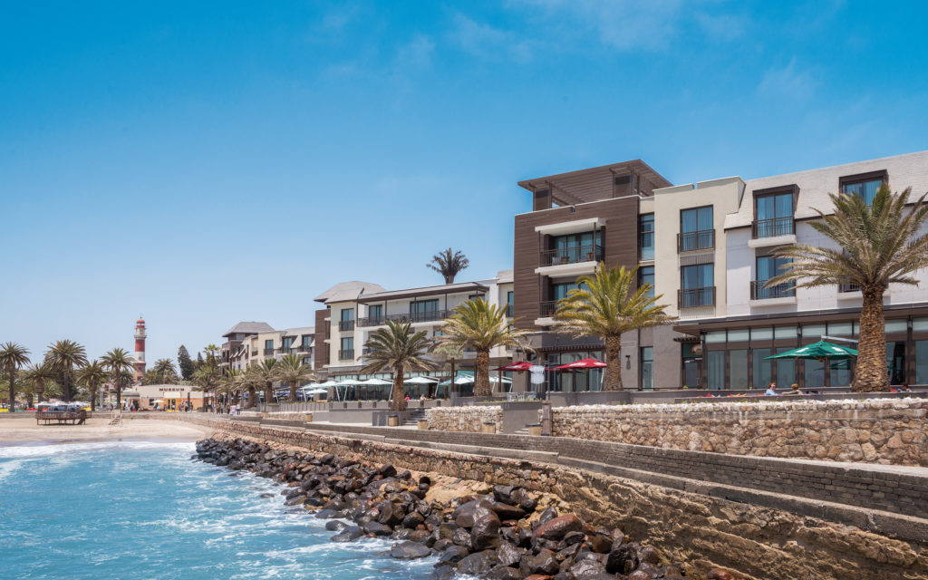 A seafront hotel with palm trees along a rocky coastal promenade