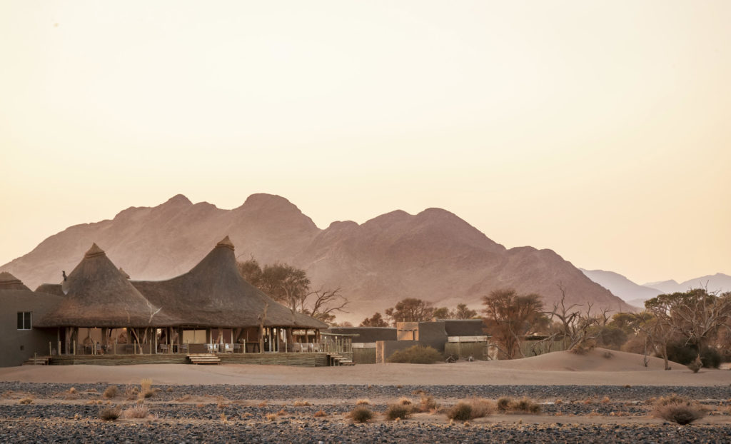 Thatched lodge buildings set against Namibian desert mountains at dusk