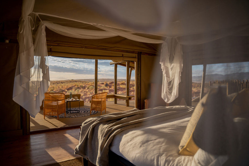 A tented suite interior with a deck and chairs overlooking open desert