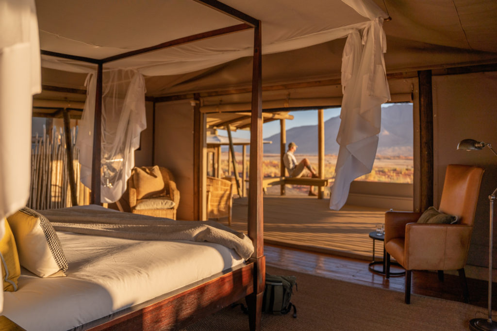 A four-poster bed inside a desert tented suite, with a guest seated on the deck beyond