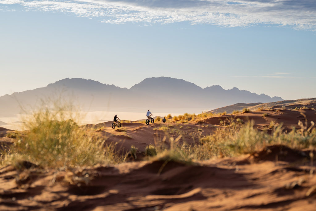 Guests fat-biking along Namibian dunes with mountains rising in the distance