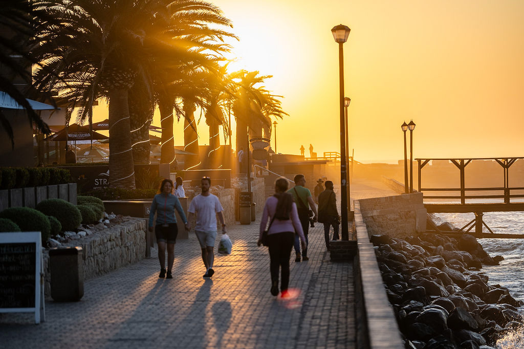 Guests walking along a palm-lined seaside promenade at sunset