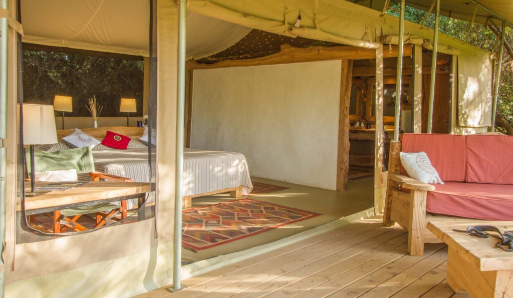 Double tent at Shompole Wilderness seen from the deck, with a kilim rug, plastered wall, pinpoint ceiling lights and a terracotta sofa.