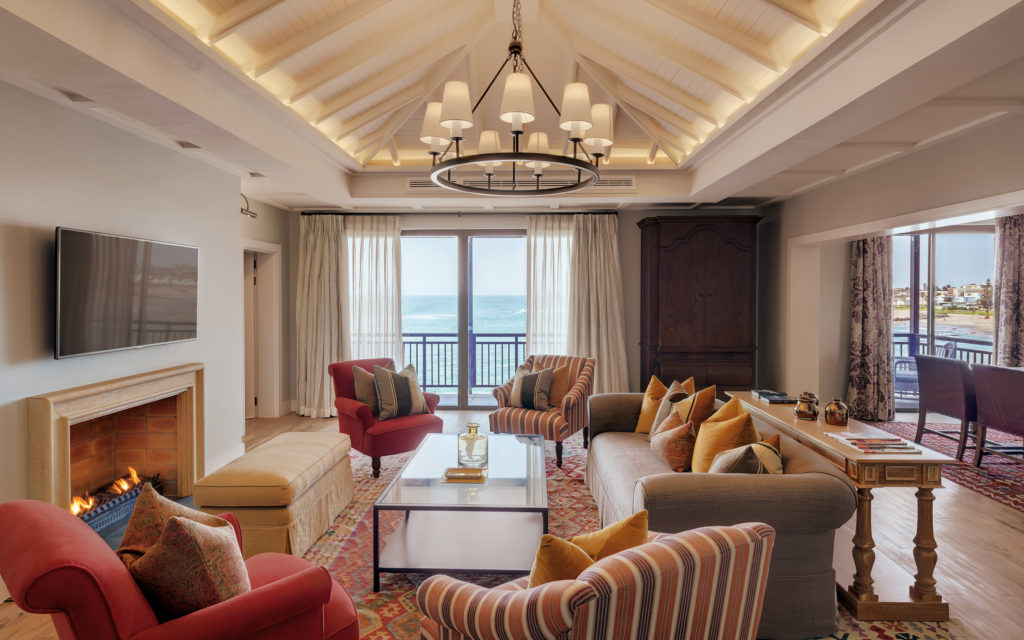 Suite lounge at Strand Hotel Swakopmund with a working fireplace, striped armchairs and glass doors opening onto the ocean