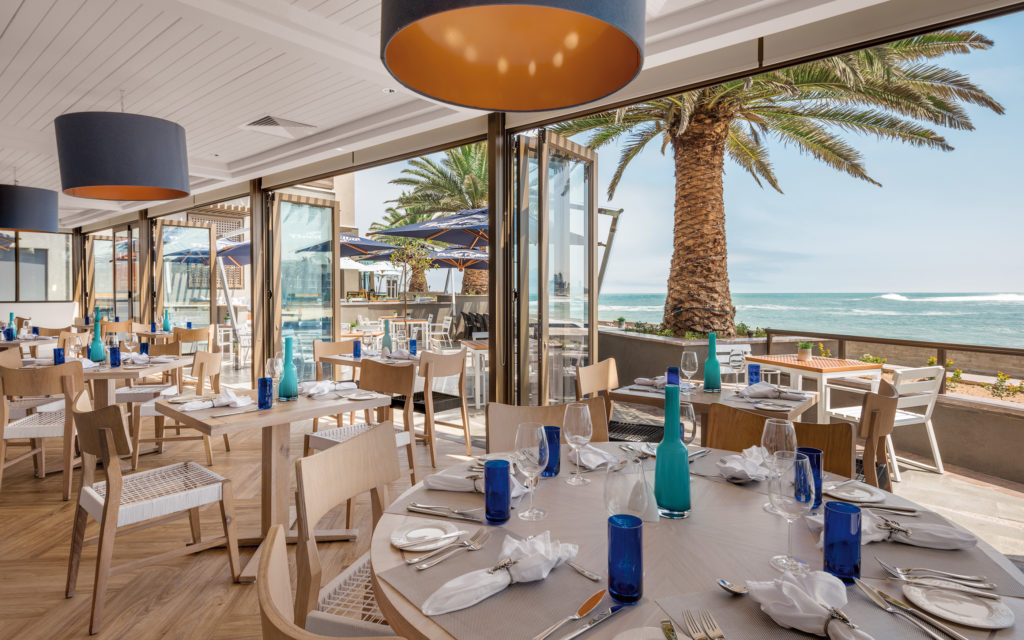 Palm-shaded terrace dining at Strand Hotel Swakopmund with ocean-blue table settings looking straight out to the Atlantic