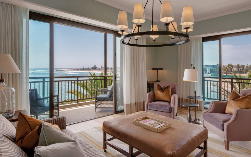 Sea-facing lounge at Strand Hotel Swakopmund with a private balcony overlooking the Atlantic, palm trees and Swakopmund's shoreline