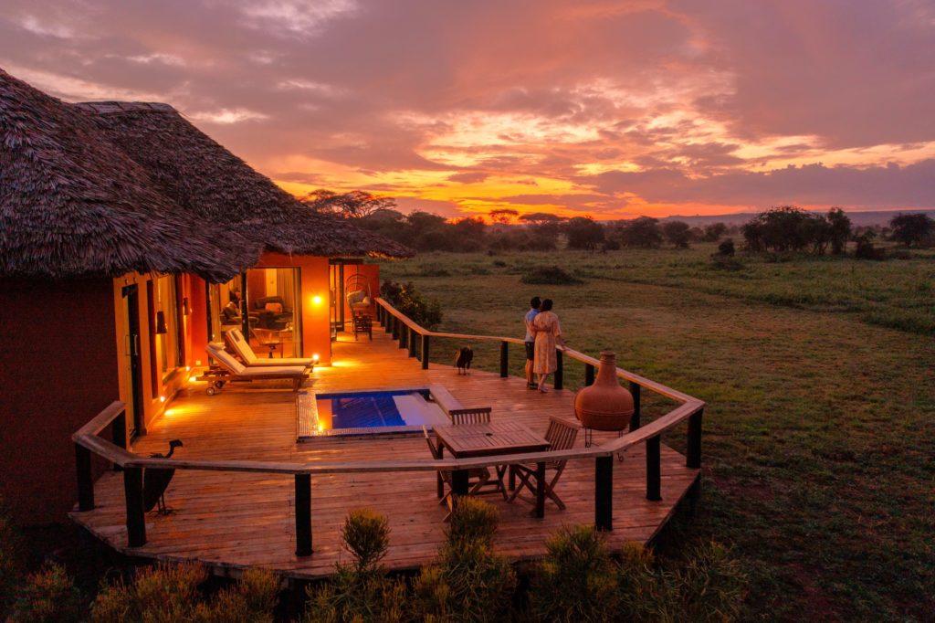 Two guests watch a fiery sunrise from a Tawi Lodge suite veranda with a plunge pool, loungers and open grassland beyond.