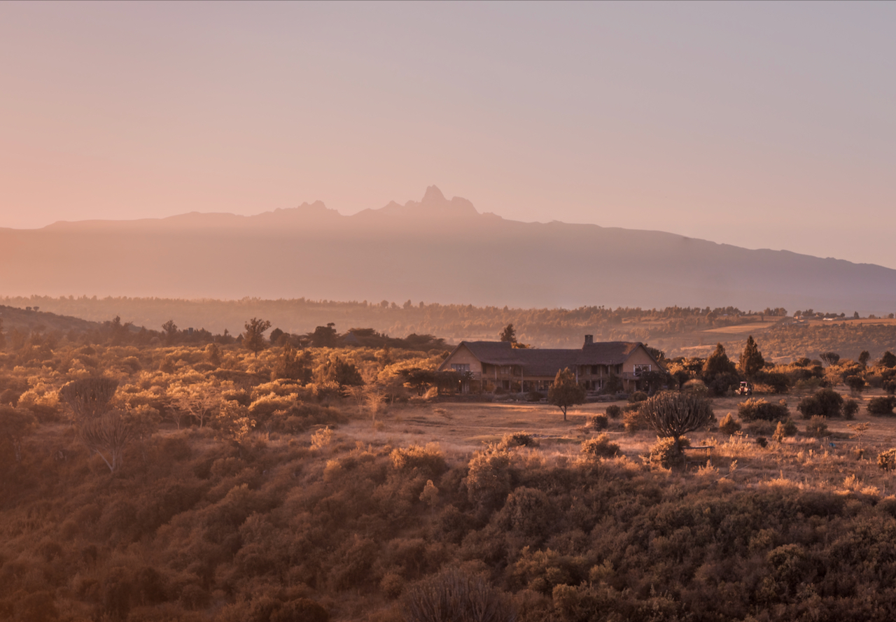 Sunrise over Olepangi Farm in Laikipia, with the main house set in bushland and the peaks of Mount Kenya outlined on the horizon.