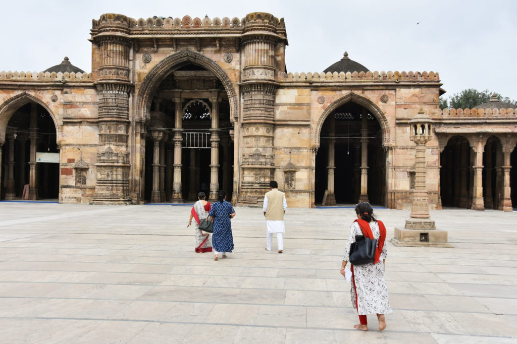 Visitors cross the marble courtyard of the Jama Masjid, its intricately carved sandstone arches rising against Ahmedabad's old city skyline.