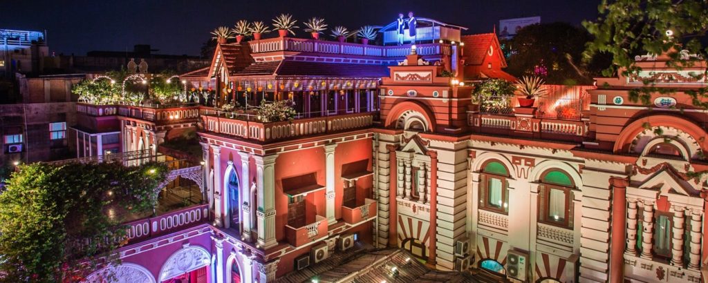 Illuminated in coloured light after dark, the hotel's terracotta rooftop terraces and colonnaded facade come alive against the night sky.