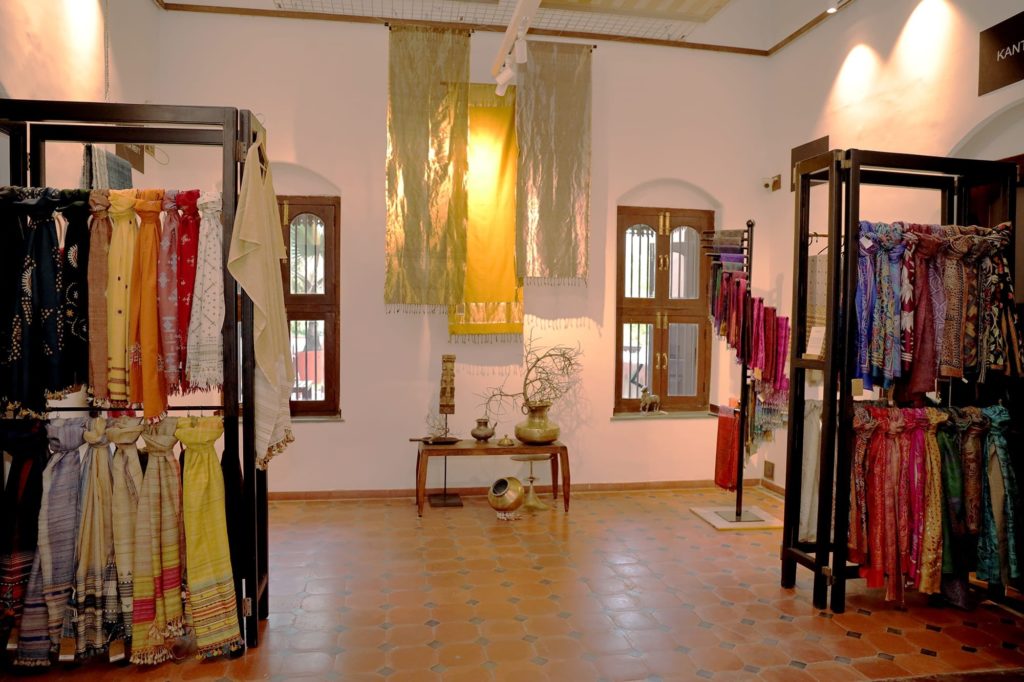 Handwoven scarves and textiles in rich jewel tones hang on display racks within the hotel's heritage textile gallery.