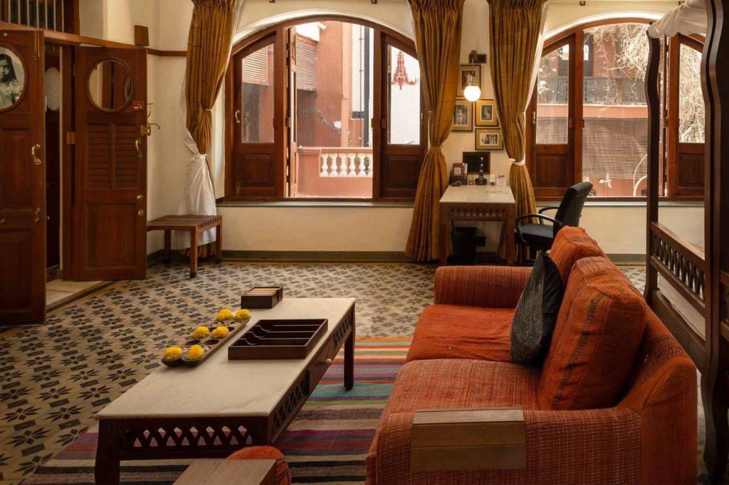 A heritage-styled suite with orange curtains, patterned tile flooring and arched windows opens onto a private balcony overlooking the old city.