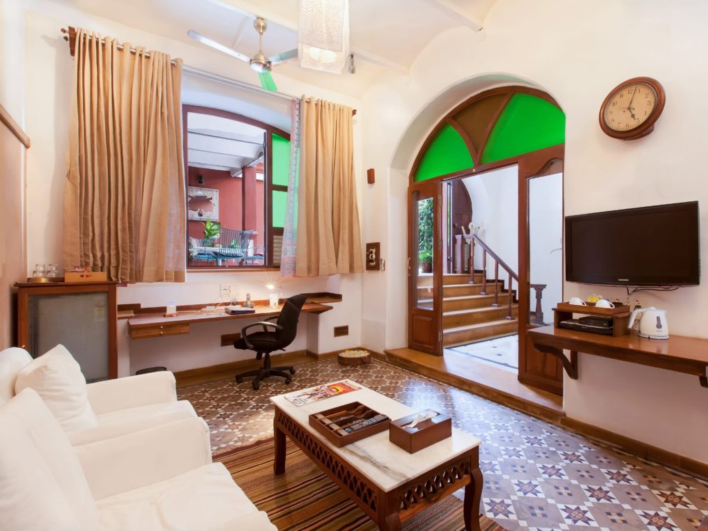 A bright sitting room with white sofas, patterned tile floor and a green stained-glass archway leads through to a wooden staircase.