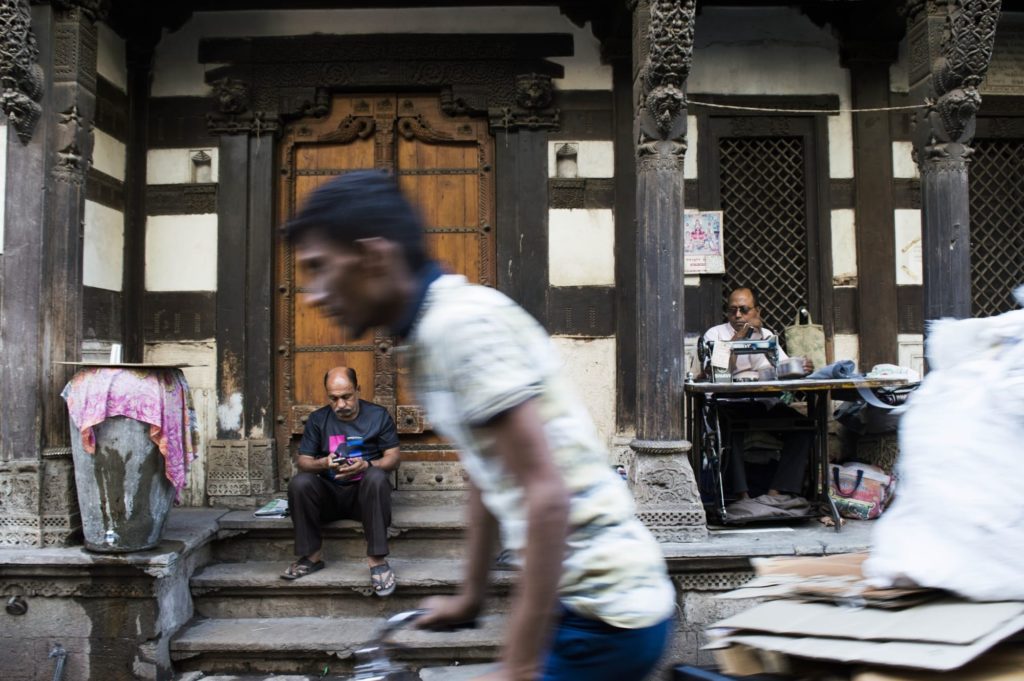 A tailor works at his sewing machine beneath the carved wooden facade of a traditional pol house in Ahmedabad's old city.