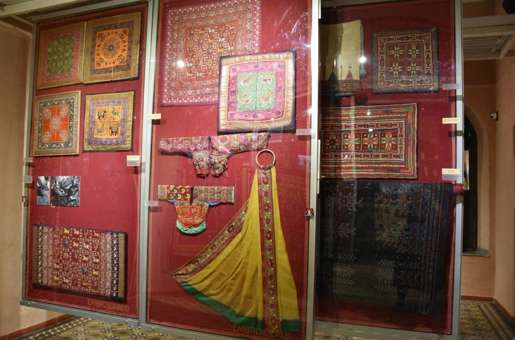 Antique embroidered textiles, garments and a golden sari hang under glass within the hotel's heritage gallery.