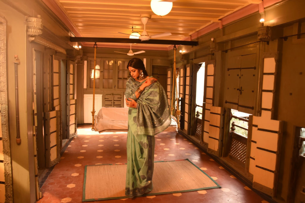 A woman in a green sari standing in a heritage wooden-shuttered corridor at The House of MG