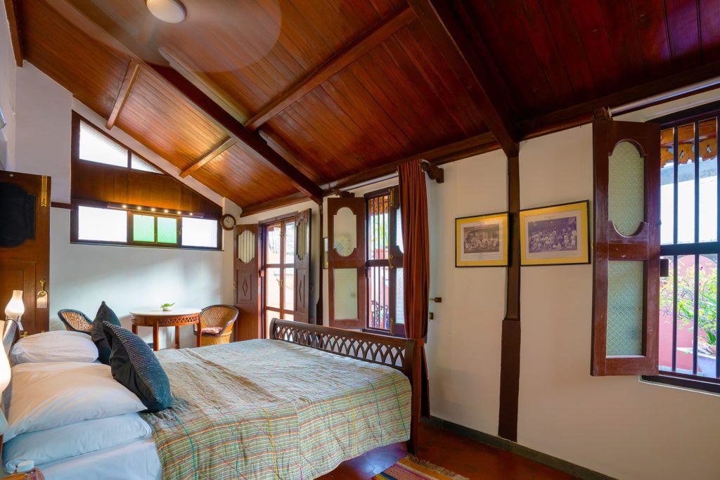 A vaulted wooden ceiling shelters a twin bedroom with a canopied daybed, writing table and vintage photographs on the walls.