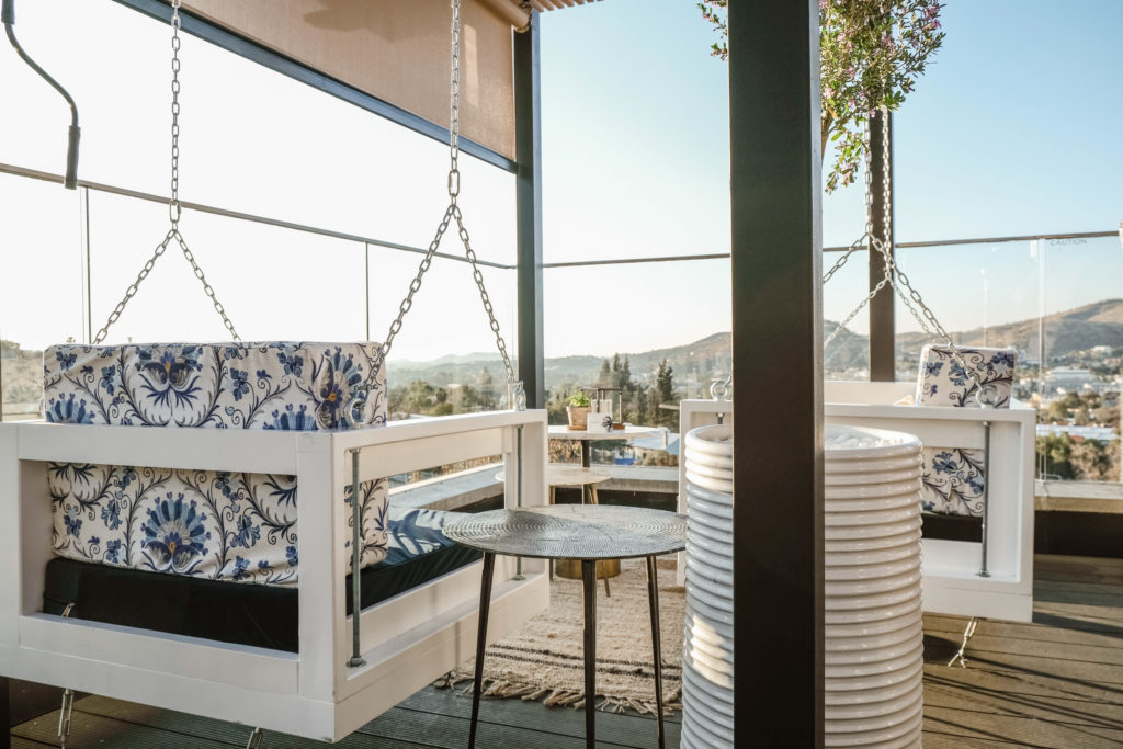 Rooftop lounge at The Weinberg with hanging swing seats upholstered in blue floral fabric overlooking the surrounding hills
