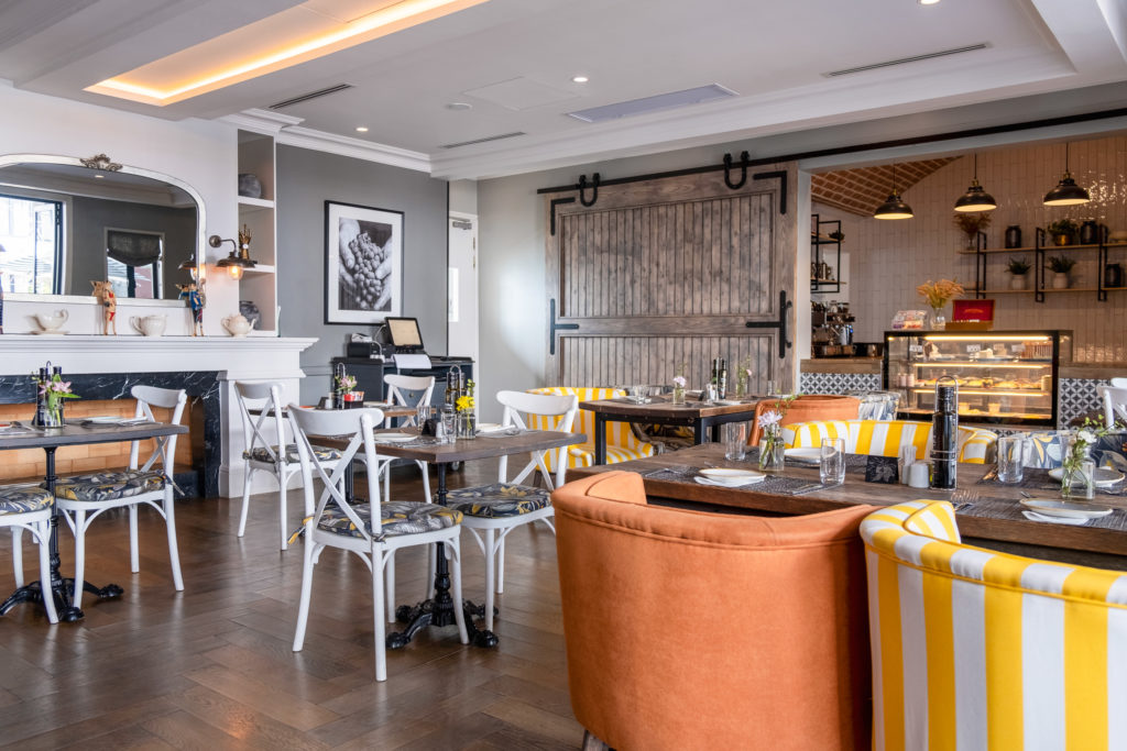 Breakfast room at The Weinberg with mismatched dining chairs, a sliding barn door and views through to the on-site café