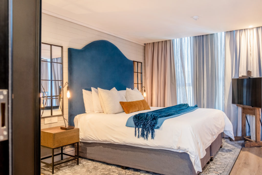 Loft bedroom at The Weinberg Windhoek with tall blue upholstered headboard and city-view window