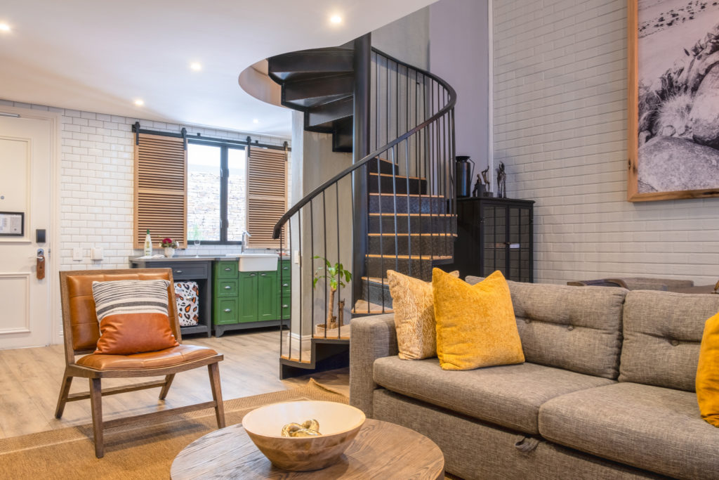 Loft suite living area at The Weinberg with spiral staircase, green kitchenette cabinetry and tufted sofa