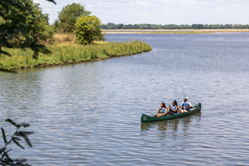 Three guests paddle a canoe along the calm waters of the Zambezi River.